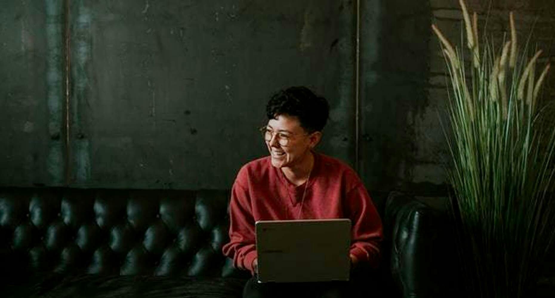 Person sitting on a black couch on their laptop smiling