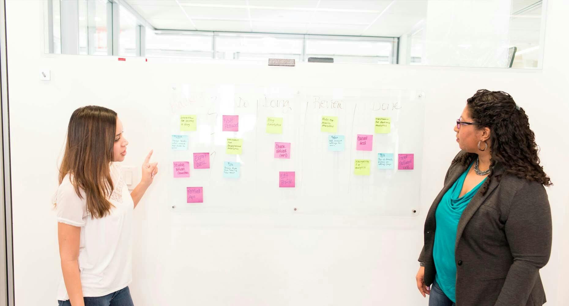 Two women working with post its on a whiteboard