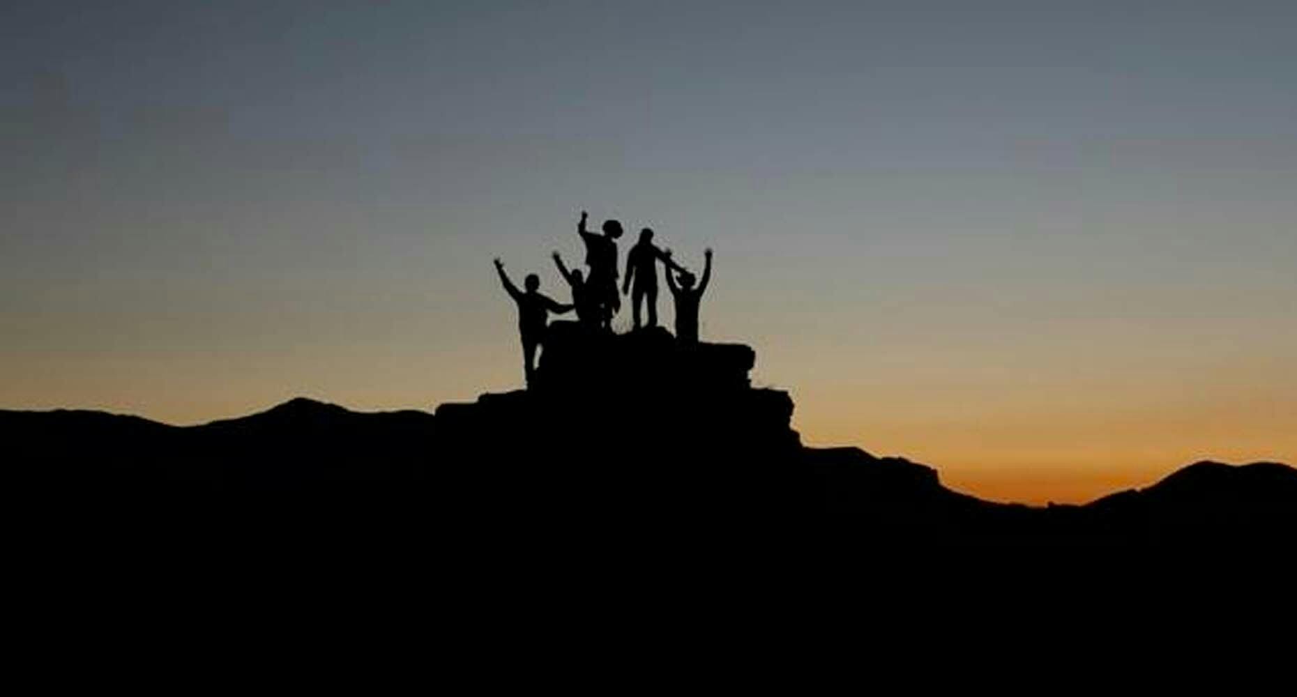 people standing at top of rocky formation at sunset